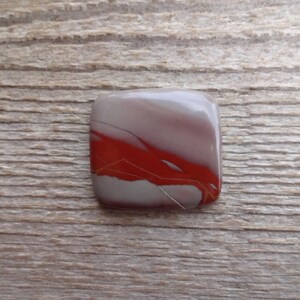 May include: A square, red, white, and gray agate cabochon with a unique pattern of veins and swirls.