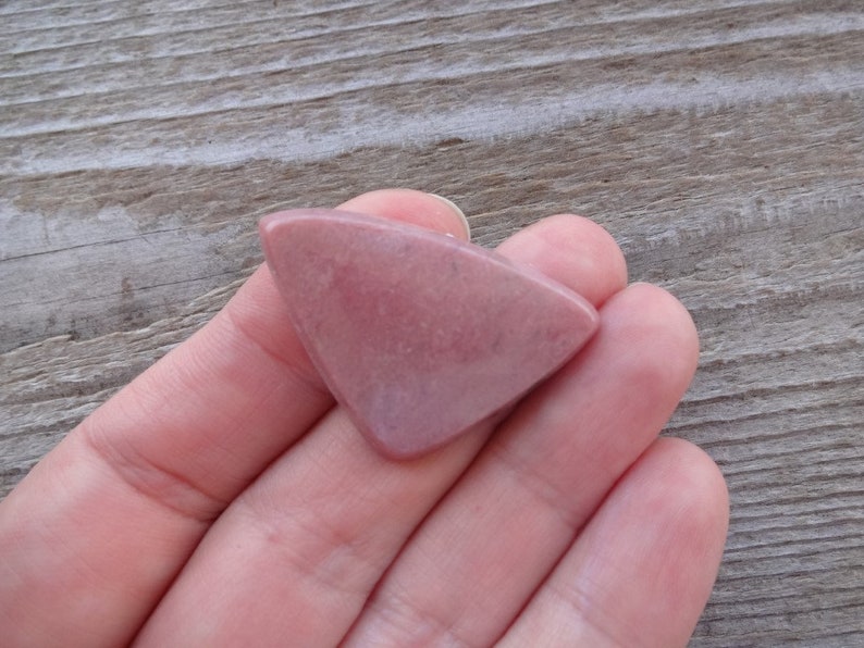May include: A triangular shaped pink and white gemstone with a smooth, polished surface.