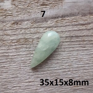 K&ouml;nnte beinhalten: Ein hellgr&uuml;ner, tropfenf&ouml;rmiger Edelstein mit den Ma&szlig;en 35x15x8mm. Der Edelstein liegt auf einer Holzoberfl&auml;che.