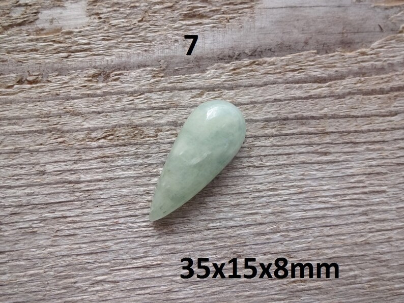 K&ouml;nnte beinhalten: Ein hellgr&uuml;ner, tropfenf&ouml;rmiger Edelstein mit den Ma&szlig;en 35x15x8mm. Der Edelstein liegt auf einer Holzoberfl&auml;che.