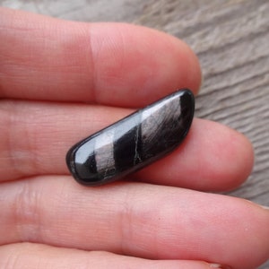 May include: A black and silver gemstone with a striated pattern. The gemstone is smooth and polished.