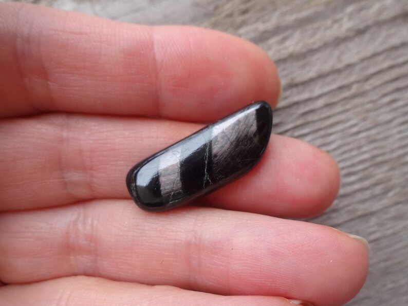 May include: A black and silver gemstone with a striated pattern. The gemstone is smooth and polished.