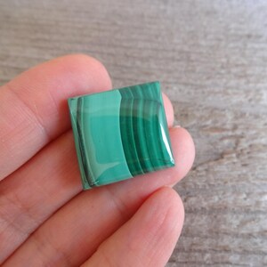 K&ouml;nnte beinhalten: Ein quadratischer gr&uuml;ner Malachit-Cabochon mit polierter Oberfl&auml;che und sichtbaren B&auml;ndern.