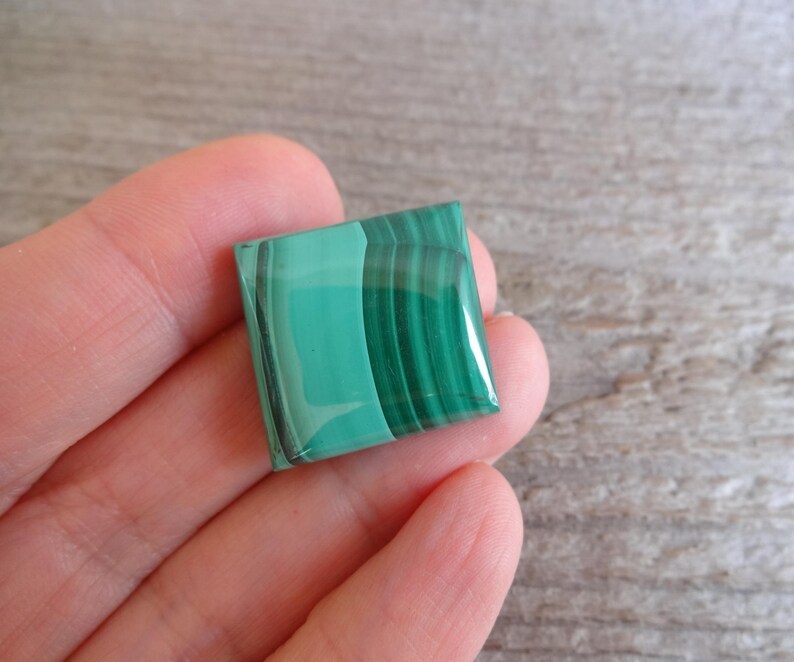 K&ouml;nnte beinhalten: Ein quadratischer gr&uuml;ner Malachit-Cabochon mit polierter Oberfl&auml;che und sichtbaren B&auml;ndern.