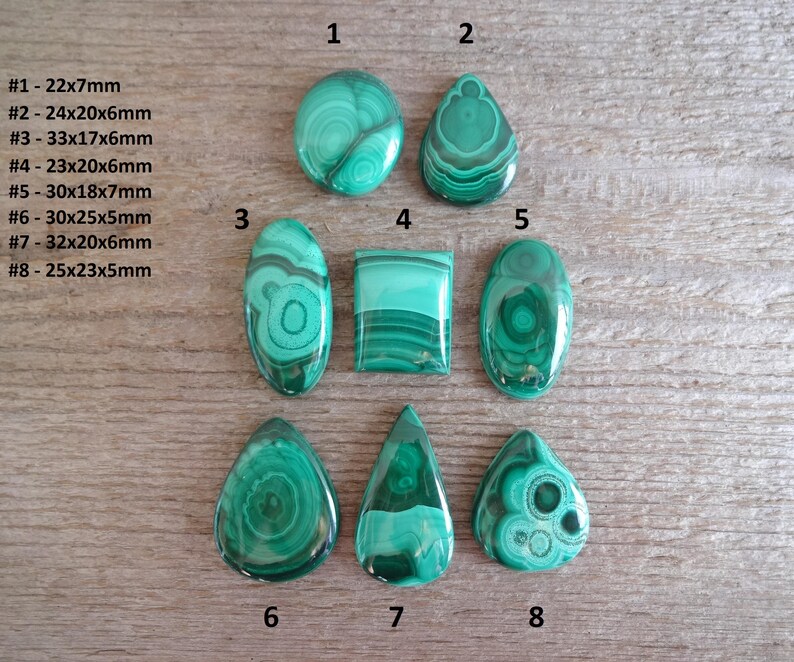 K&ouml;nnte beinhalten: Acht polierte Malachit-Cabochons in verschiedenen Formen und Gr&ouml;&szlig;en, darunter rund, oval und tropfenf&ouml;rmig. Die Cabochons sind in einem leuchtenden Gr&uuml;n mit komplizierten Mustern aus dunklerem Gr&uuml;n und Schwarz.