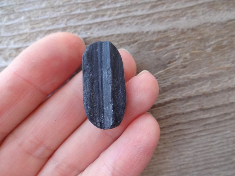 May include: A black oval-shaped stone with a thin, white line running down the center.