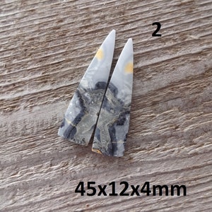 Puede incluir: Dos piedras triangulares pulidas con un patr&oacute;n veteado gris, negro y amarillo. Las piedras est&aacute;n sobre un fondo de madera envejecida. El texto "2" est&aacute; encima de las piedras y "45x12x4mm" debajo.
