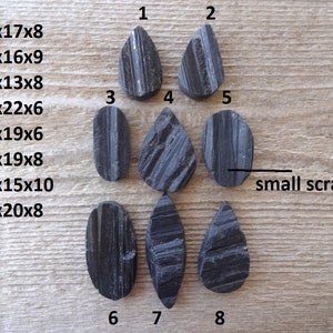 May include: Eight black obsidian teardrop and oval shaped stones with measurements listed next to each stone. The stones are arranged in two rows on a wooden surface. The text "small scratch" is written on the right side of the image.