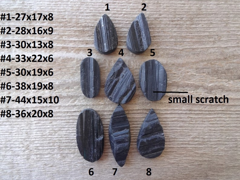 May include: Eight black obsidian teardrop and oval shaped stones with measurements listed next to each stone. The stones are arranged in two rows on a wooden surface. The text "small scratch" is written on the right side of the image.