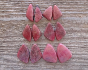 May include: Eight pink and white, teardrop-shaped, polished stones. The stones are arranged in two rows of four.
