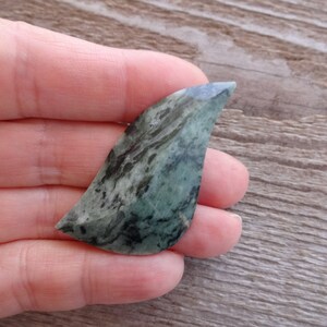 Puede incluir: Una piedra verde y negra con vetas, con una punta puntiaguda, con forma de hoja. La piedra es lisa y pulida.