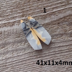 Puede incluir: Dos colgantes alargados de piedra pulida con un patr&oacute;n gris claro, negro y amarillo. Los colgantes est&aacute;n etiquetados con el n&uacute;mero "1" y miden 41x11x4mm.