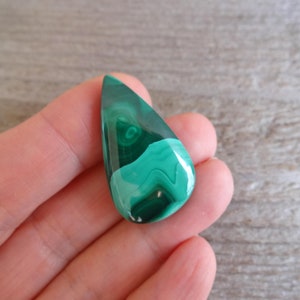 K&ouml;nnte beinhalten: Ein tropfenf&ouml;rmiger gr&uuml;ner Malachit-Cabochon mit wirbelnden Mustern.