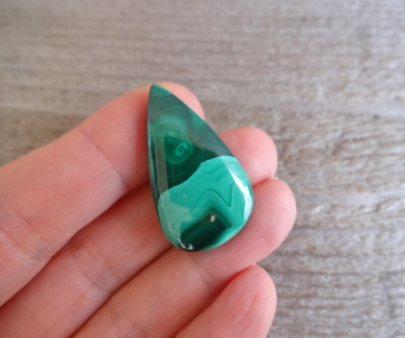 K&ouml;nnte beinhalten: Ein tropfenf&ouml;rmiger gr&uuml;ner Malachit-Cabochon mit wirbelnden Mustern.