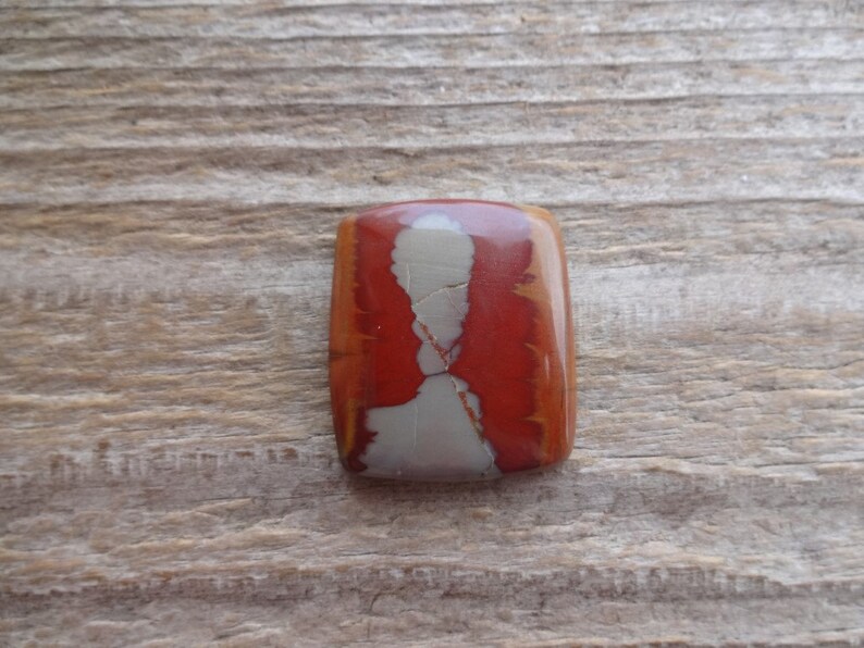 May include: A rectangular cabochon of red, white, and brown jasper with a swirling pattern.