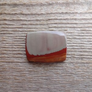 May include: A smooth, rectangular cabochon of red, white, and orange banded jasper. The stone has a polished finish and is set in a bezel.