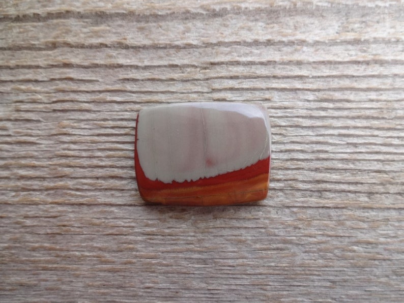 May include: A smooth, rectangular cabochon of red, white, and orange banded jasper. The stone has a polished finish and is set in a bezel.