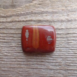 May include: A square, red, orange, and white gemstone cabochon with a polished finish. The stone has a unique pattern of white and orange lines.