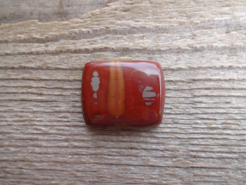 May include: A square, red, orange, and white gemstone cabochon with a polished finish. The stone has a unique pattern of white and orange lines.