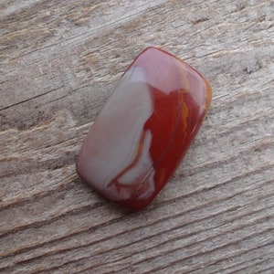 May include: A smooth, polished, red and white agate stone with a rectangular shape.