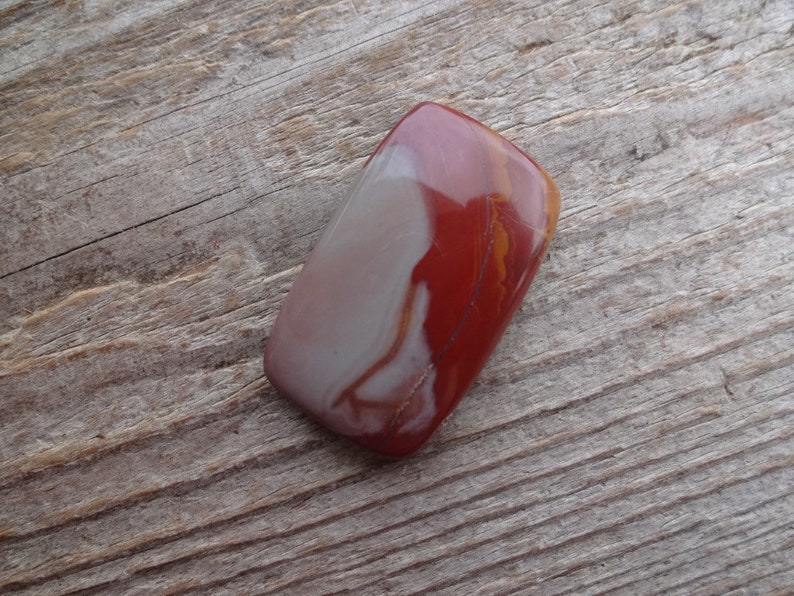 May include: A smooth, polished, red and white agate stone with a rectangular shape.