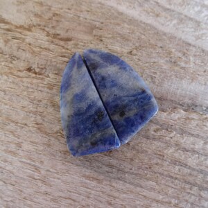 K&ouml;nnte beinhalten: Zwei St&uuml;cke aus blauem und wei&szlig;em Lapislazuli-Stein, in Dreiecksform geschnitten. Die Steine sind glatt und poliert.