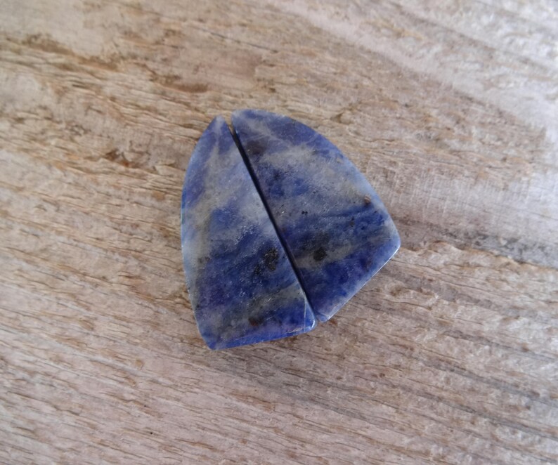 K&ouml;nnte beinhalten: Zwei St&uuml;cke aus blauem und wei&szlig;em Lapislazuli-Stein, in Dreiecksform geschnitten. Die Steine sind glatt und poliert.