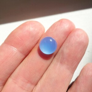 Puede incluir: Una piedra preciosa redonda de color azul claro, probablemente calcedonia, mostrada en un dedo.