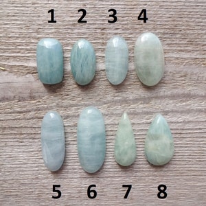 K&ouml;nnte beinhalten: Acht Aquamarin-Cabochons in verschiedenen Formen und Gr&ouml;&szlig;en, nummeriert von 1 bis 8. Die Steine sind hellblaugr&uuml;n und haben eine glatte, polierte Oberfl&auml;che.