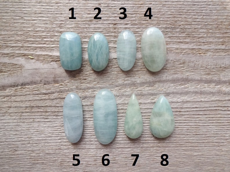K&ouml;nnte beinhalten: Acht Aquamarin-Cabochons in verschiedenen Formen und Gr&ouml;&szlig;en, nummeriert von 1 bis 8. Die Steine sind hellblaugr&uuml;n und haben eine glatte, polierte Oberfl&auml;che.