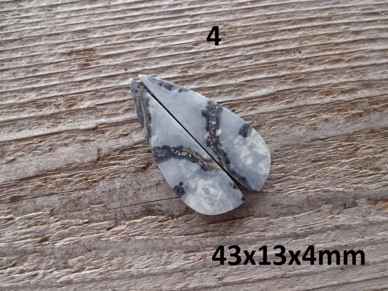 Puede incluir: Dos piedras pulidas en forma de l&aacute;grima, con un patr&oacute;n veteado gris y blanco y vetas negras. Las piedras se muestran sobre una superficie de madera. El texto "4" est&aacute; encima de las piedras y "43x13x4mm" debajo.