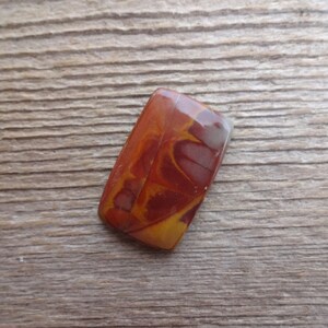 May include: A rectangular, polished stone cabochon with a swirling pattern of red, orange, and white.