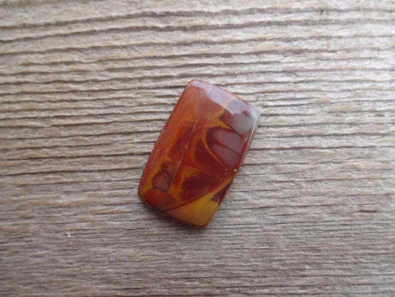 May include: A rectangular, polished stone cabochon with a swirling pattern of red, orange, and white.