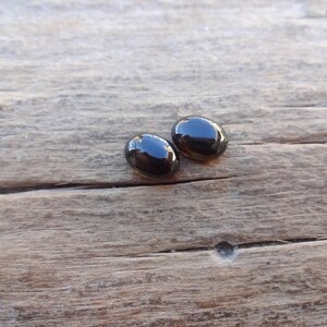 May include: Two black oval-shaped gemstones on a wooden surface.