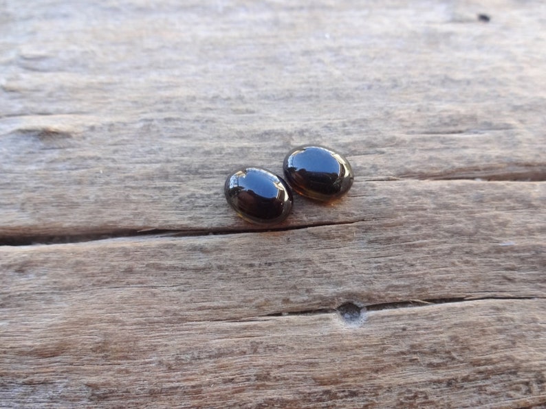May include: Two black oval-shaped gemstones on a wooden surface.