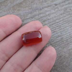 Puede incluir: Una gema rectangular transl&uacute;cida de color &aacute;mbar. La piedra tiene bordes redondeados y una superficie pulida, que refleja la luz. La gema es probablemente un cabuj&oacute;n, adecuado para joyer&iacute;a u otros usos decorativos.