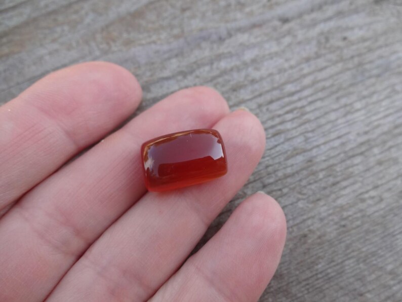 Puede incluir: Una gema rectangular transl&uacute;cida de color &aacute;mbar. La piedra tiene bordes redondeados y una superficie pulida, que refleja la luz. La gema es probablemente un cabuj&oacute;n, adecuado para joyer&iacute;a u otros usos decorativos.