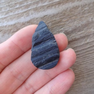 May include: A black teardrop-shaped obsidian stone with striations.