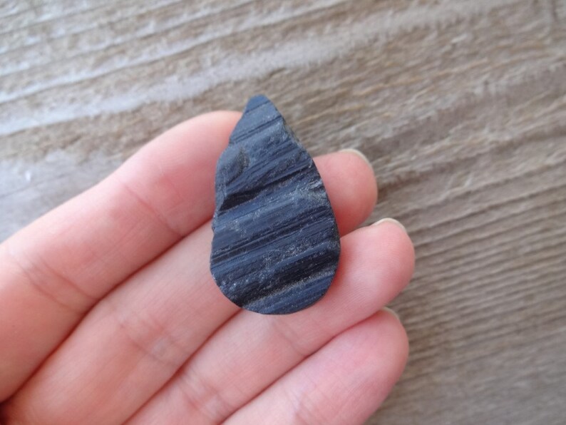 May include: A black teardrop-shaped obsidian stone with striations.