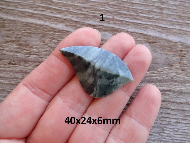 Puede incluir: Un cabuj&oacute;n de piedra verde y negro con forma curva. La piedra mide 40x24x6mm.