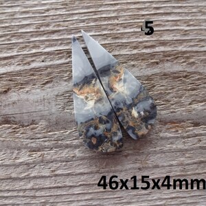 Puede incluir: Dos piedras a juego, en forma de l&aacute;grima, con un patr&oacute;n veteado de gris, negro y marr&oacute;n. Las piedras est&aacute;n etiquetadas con el n&uacute;mero "5" y las dimensiones "46x15x4mm". El fondo es una superficie de madera envejecida.