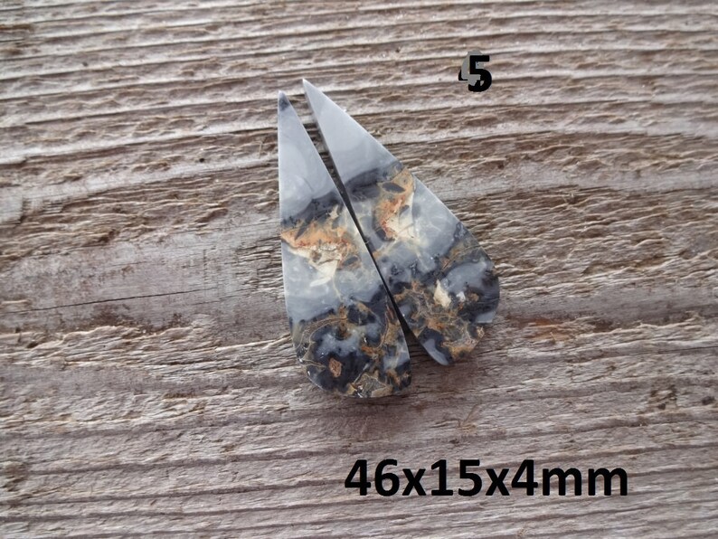 Puede incluir: Dos piedras a juego, en forma de l&aacute;grima, con un patr&oacute;n veteado de gris, negro y marr&oacute;n. Las piedras est&aacute;n etiquetadas con el n&uacute;mero "5" y las dimensiones "46x15x4mm". El fondo es una superficie de madera envejecida.