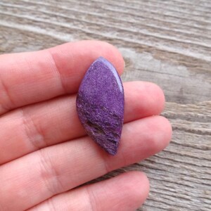 May include: A purple and white cabochon gemstone with a rough, textured surface.