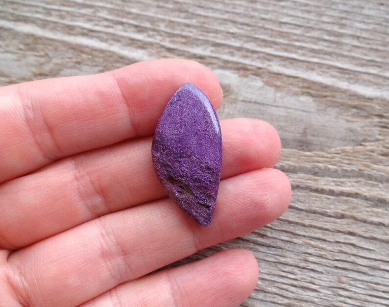 May include: A purple and white cabochon gemstone with a rough, textured surface.