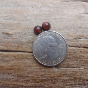 May include: Two small, round, red-brown cabochon gemstones, approximately the size of a US quarter.