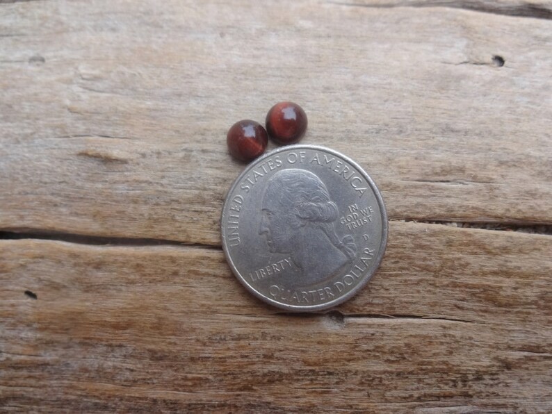 May include: Two small, round, red-brown cabochon gemstones, approximately the size of a US quarter.