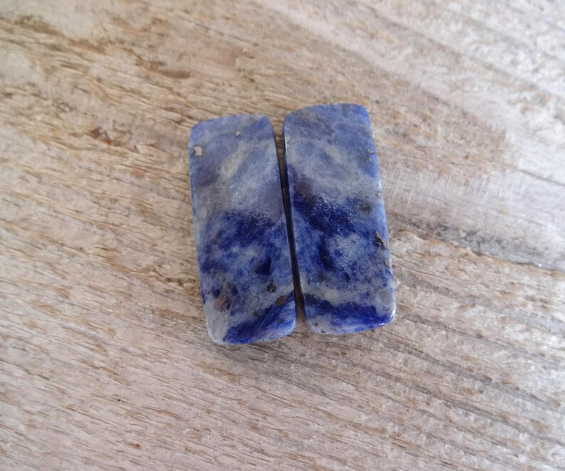 K&ouml;nnte beinhalten: Zwei rechteckige St&uuml;cke aus blauem und wei&szlig;em Lapislazuli-Edelstein. Die Steine haben ein marmoriertes Muster und sind glatt und poliert.