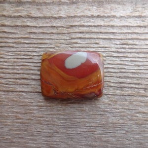 May include: A square, red, orange, and white jasper cabochon with a swirling pattern.