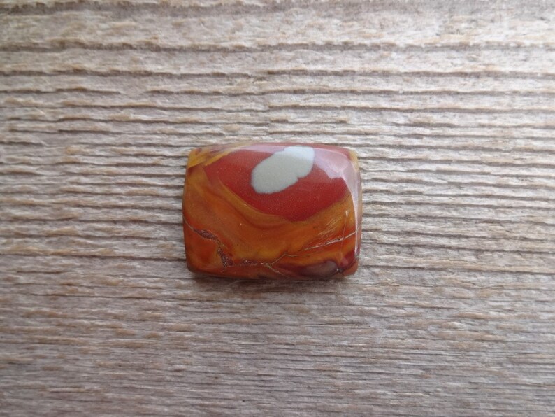 May include: A square, red, orange, and white jasper cabochon with a swirling pattern.