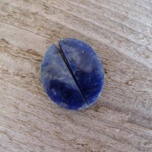 K&ouml;nnte beinhalten: Zwei H&auml;lften eines blauen Lapislazuli-Steins, jede in Form eines Halbkreises, liegen nebeneinander auf einer Holzoberfl&auml;che.